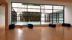 Grande salle de repos en parquet avec une immense façade vitrée donnant sur un bassin d'eau.
