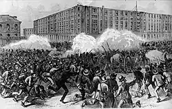 Gravure d'une scène de combat urbain. Une foule d'hommes en civil et armés de fusils à baïonnette chargent un groupe de soldats entourant plusieurs canons. Des bâtiments en briques à plusieurs étages sont visibles à l'arrière-plan malgré la fumée.