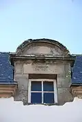 Photographie d'une lucarne arrondie, sur fond de toit en ardoise.