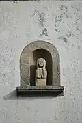 Photographie d'une niche de façade en granit, contenant une statuette.