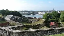 Vue en surplomb de remparts dominant un cours d’eau.