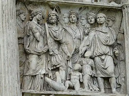 un groupe d'une dizaine d'hommes et de femmes en pied ; deux enfants nus au sol, le visage supprimé.