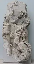 homme barbu bras levé devant une statuette