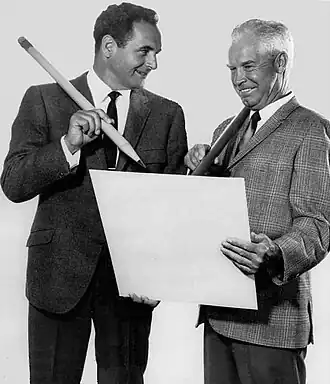 photgraphie en noir et blanc de deux hommes souriants et tenants en main des crayons gigantesques