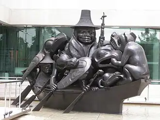 Sculpture d'une personne sur un bateau accompagnée d'une multitude d'animaux stylisés, qui occupent tout le pont. Le groupe rame.