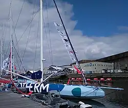 Vu de trois quarts avant, voilier bleu sombre et bleu clair amarré au ponton.
