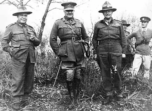 Trois officiers debout posant pour une photograhie, avec deux autres soldats au fond à droite.