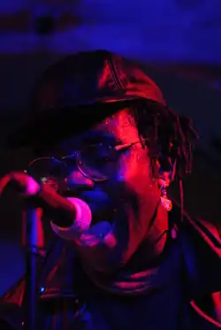 Homme qui chante, le micro devant lui. Image en couleur rouge et bleue.