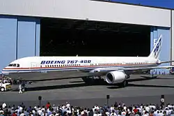 Vue latérale d'un avion de ligne biréacteur devant un hangar avec de la foule autour.