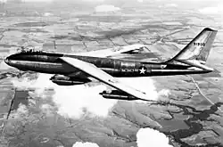 Vue latérale gauche d'un avion à réaction en vol au-dessus des plaines ; la flèche des ailes est mise en évidence, de même que les réacteurs suspendus sous celles-ci.