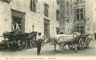 Photographie en noir et blanc d'une charrette tirée par des bœufs dans la cour d'un château.