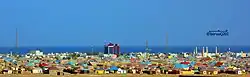 Photographie couleurs panoramique de constructions basses colorées. À l'horizon, la mer et un navire