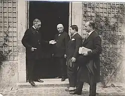 Groupe de personnages discutant sur le pas d'une porte.