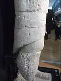 Détail de statue blanche, la forme est très cylindrique, sculptée d'une « jupe » plus longue à l'arrière (à gauche).