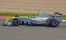 Vue de gauche d'une monoplace de Formule 1 blanche, aux liserés jaune fluo et noir, en piste