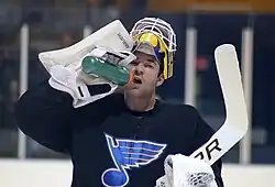 Photographie d'un gardien de but de hockey sur glace avec un maillot noir en train de boire de l'eau dans une gourde.