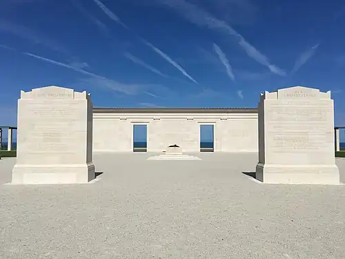 Photo de deux monuments quadrangulaires devant un mur percé de deux ouvertures donnant sur la mer.