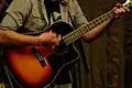 Une personne casse une corde de La sur sa guitare folk en jouant en strumming.