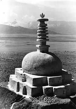 Photographie en noir et blanc d'un monument en pierres surmonté d'une colonne composée de disques circulaires.