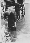 Une femme âgée ramasse des déchets jetés d'un chariot de marchand de légumes, en 1923.