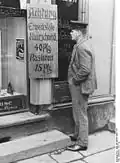 Un homme lit un panneau « Attention, chômeurs, coupe de cheveux 40 pfennigs, barbe 15 pfennigs », en 1927.