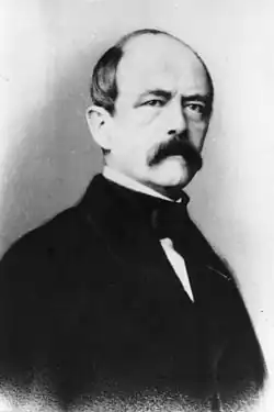 Portrait photographique d'un homme chauve portant une moustache épaisse.