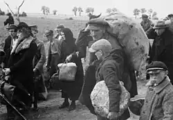 Photographie en noir et blanc d'hommes, femmes et enfants portant quelques colis et marchant dans la même direction.