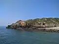Mer calme, ciel bleu dégagé. Au centre de l'image, petite falaise s'enfonçant doucement dans la mer.