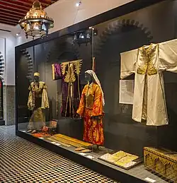 Un exemplaire de caftan de Tétouan de forme rectangulaire légèrement évasé vers le bas, ouvert sur le devant, aux manches longues et larges. Des boutons coniques en passementerie en assurent la fermeture vers le haut.
