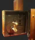 Cinématographe vu de l'arrière (couvercle ouvert). On voit le couloir du film et la fenêtre de cadrage du film. La manivelle est mise ici en décoration. Normalement, elle traverse la couvercle arrière (visible à droite).