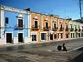 Une rue dans la ville de Campeche. Des maisons de même hauteur mais de couleurs différentes sont alignées en arrière-plan. En bas à droite de l'image est garé un scooter.
