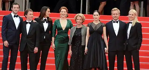 Photographie au format paysage et en couleurs de plusieurs personnes en tenue de gala, posant en souriant sur un tapis rouge.
