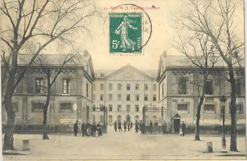 Une grille d'entrée entre deux corps de garde, donnant sur une vaste cours, cette dernière fermée en arrière-plan par un bâtiment de quatre étages.