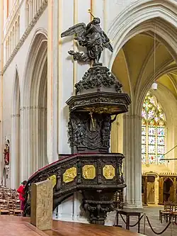 Photographie d'une chaire à prêcher en bois ornée de panneaux sculptés dorés.