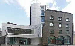 Un bâtiment en briques rouges, avec une extension moderne sur sa gauche, de couleur blanche.