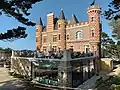 La façade ouest du château du Nessay avec sa terrasse au-dessus du restaurant qui abrite une belle collection de dame-jeanne derrière la vitre.