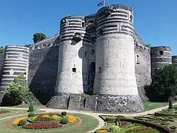 Photographie du château : deux tours et des jardins dans les douves au premier plan.