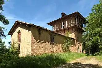 photo couleur d'un bâtiment allongé ressemblant à une grange. Il est appuyé à une tour carrée ceinturée d'une galerie en bois.
