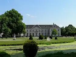 Bâtiment au second plan derrière un parc avec buis et bassin d'eau