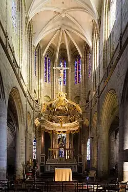 Photographie d'un chœur d'église avec des murs en pierre beige surmontés de voûtes en pierre blanche.