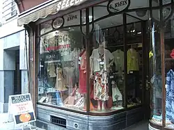 Vitrine située à la rue Neuve, dessinée par Hector Tonet. Enlevé en 2017 elle retrouve sa place en 2019 en façade du nouvel immeuble construit à cet endroit.