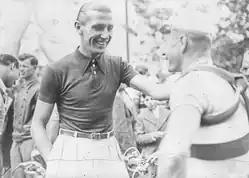 Photographie en noir et blanc montrant un homme en civil posant sa main sur l'épaule d'un coureur cycliste.