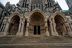 Photographie du triple portail d'une cathédrale, surmontant des marches.