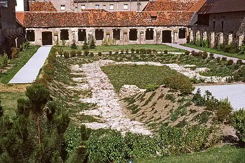 Photographie couleur d'une cour excavée entourée d'un cloître, dont toutes les baies ont disparu.