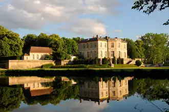 Vue au fond d'un château, se reflétant dans une pièce d'eau. Au même niveau, sur la gauche, une batisse.