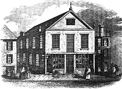 Une gravure en noir et blanc représentant une scène de rue avec, au centre, une église de 2,5 étages avec des fenêtres à meneaux.