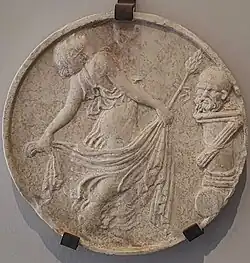 Plaque ronde montrant une danseuse cambrée avec voile & une tête sur une colonne.