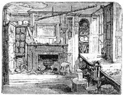 Les fenêtres permettent la diffusion de la lumière. Une cheminée entourée de diverses armoires et récipients domine la pièce. Du plâtre manque au plafond. Le sol parait constitué de planches de bois.