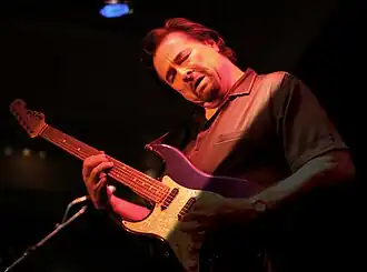 Photographie de Coco Montoya en concert, jouant de la guitare la tête penchée et les yeux fermés.