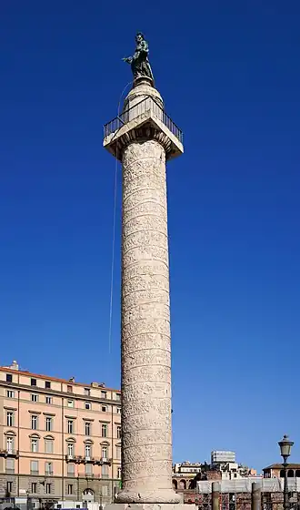 haute colonne blanche, droite et décorée d'une spirale, surmontée d'une petite plate-forme carrée où repose une statue d'homme.